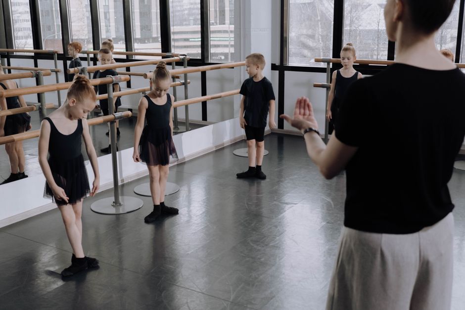 Young ballet students practicing in a bright studio with an instructor guiding them.