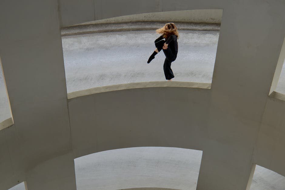 A dancer performs gracefully in a modern, concrete urban environment.
