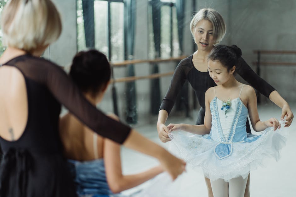 Content Asian ballet teacher and cute girl ballerina looking in mirror and touching fluffy tutu skirt during ballet class in studio